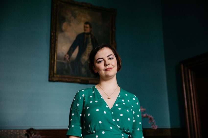 Alice Procter stands in front of a portrait of Matthew Flinders at Ayers House Museum 